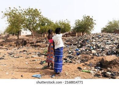 Two African girls pointing to the mountain of garbage that occupies the street of their village indicating the mismanagement of waste that afflicts their continent - Shutterstock ID 2168814771
