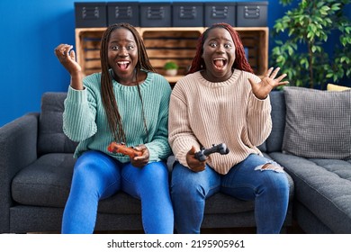 Two african woman playing video game holding controller celebrating victory with happy smile and winner expression with raised hands  - Shutterstock ID 2195905961