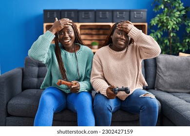 Two african woman playing video game holding controller stressed and frustrated with hand on head, surprised and angry face  - Shutterstock ID 2302427159