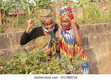 Two African Women Looking Into Their Phone In The Farm