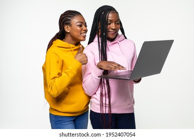 Two African Young People Standing Perplexed In Red And Black Clothes Holding, And Using A Laptop While Smiling Isolated On White Background