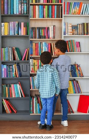Two afro american children look for books in bookshelves and read together in school library or bookstore. Elementary School. Back to school.