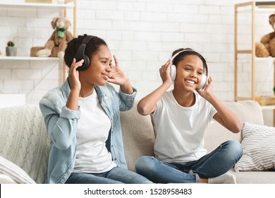 Two afro schoolgirls listening to music with wireless headphones and dancing at home, empty space
