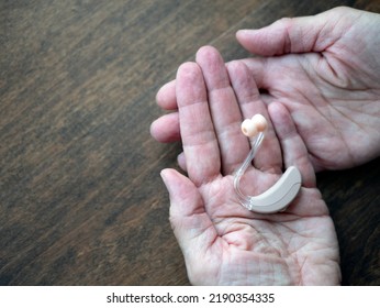 Two Aged Hands Hold A Hearing Device, Copy Space. Concept Of The Hearing Loss. Assistive Technology