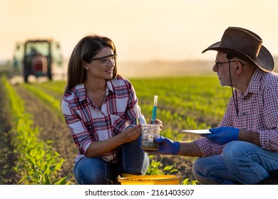 Two agronomists young woman and senior man experimenting with chemicals on soil in corn field in spring time as plant protection concept. Tractor working in background - Powered by Shutterstock