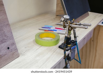 Two airbrushes on metal base near adhesive tape and several markers on wooden table, arts class, horizontal photo