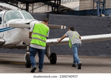 Two aircraft maintenance assistants help park a small airplane in a hangar - Powered by Shutterstock