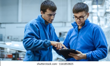 Two aircraft maintenance mechanics have a conversation while using a tablet in a plane hangar. - Powered by Shutterstock