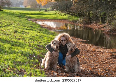 Two Airedale terriers in a leafy country location. A lady cuddles her dogs. - Shutterstock ID 2395029519