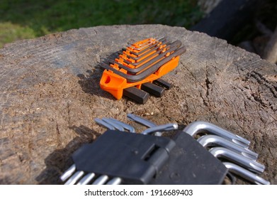 Two allen wrench sets on a wooden log. Silver and metal allen key sets available in many different sizes. Small handheld tools used for for driving bolts and screws with a hexagonal socket.