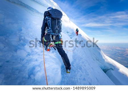 Two alpinists mountaineers climbing ascending over ice snow crevasse crack, extreme sport  mountain climbing. Mont Blanc massif, Europe travel tourism.