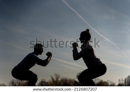Two amazing and attractive fit friends are doing squad exercise on the grass, silhouette