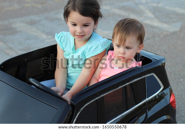 Two\
amazing girls ride in one big toy car on city street asphalt.\
Outdoor driving in a summer attraction for\
children