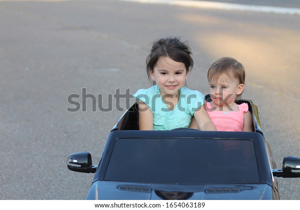 Two
amazing girls ride in one big toy car on city street asphalt.
Outdoor driving in a summer attraction for
children