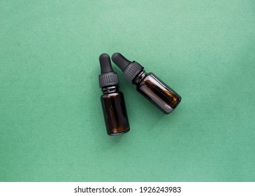 two Amber glass dropper bottle with essential oil for hair or face care on green background. Flat lay, top view. Cosmetic packaging mockup. Flat lay, top view, overhead.