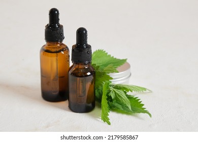 two amber Glass dropper bottles of nettle oil or serum and nettle leaves beige background top view opy space nettle benefits for skin, natural cosmetics concept