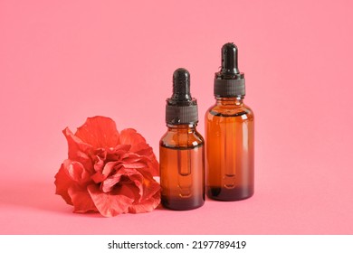 Two Amber Glass Dropper Bottles And Hibiscus Flower On Pink Background Copy Space Mock Up, Serum Or Oil With Hibiscus Extract