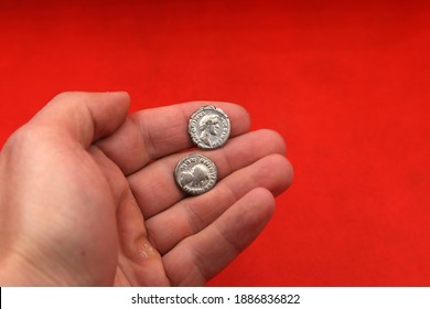 Two Ancient Roman Silver Coins In Hand On Red Background