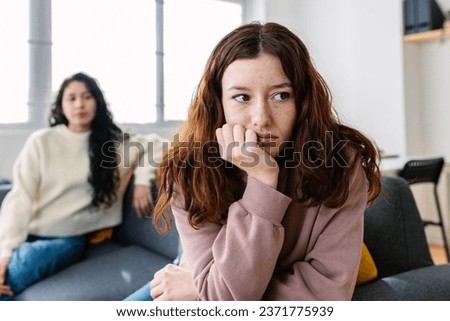 Two angry female friends sitting separately on sofa at home after an argument