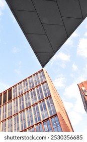 Two angular buildings barely touch at their corners via forced perspective, creating a strong contrast both with each other and the clear blue sky above.