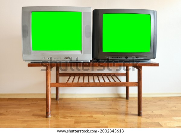 Two antiquated\
vintage TVs with blank green screens sit on a vintage table in a\
1990s tenement building.