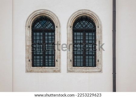 Two antique old windows with black iron bars framed on a light grey wall. The Jesuit Church in Lviv.