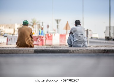 Two Arab Construction Workers Taking Brake And Sitting On The Sidewalk In Dubai, United Arab Emirates