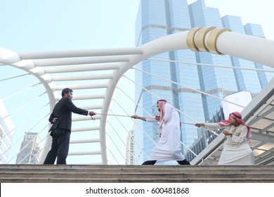 Two Arab man is vigorously pulling the rope from the one end while a man in dark business suit  is holding another end of the rope,competitor concept.