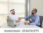 Two arab men business team working colleagues in office or meeting room with laptop wearing traditional and casual expat and UAE national showing diversity shaking hands closing a deal