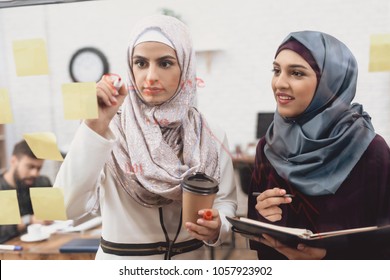 Two Arab Women In Hijab Working In Office. Coworkers Are Taking Notes On Glass Board.