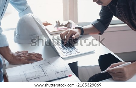 Two  architect colleagues discussing data working on digital tablet and laptop computer with architectural project at construction site on desk at office