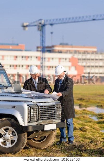 Two architect developers reviewing building plans at\
construction site