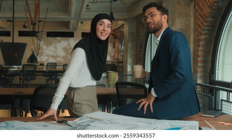 Two architects contractors engineers colleagues architecture project Arabian muslim designers man woman in hijab discuss blueprint draft of office building businessman businesswoman drink coffee smile - Powered by Shutterstock