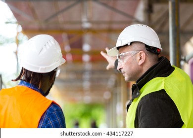 Two architects wearing hardhat and safety jacket pointing at scaffolding on construction site - Shutterstock ID 434117227