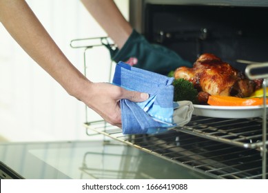 Two Arms Of A Woman Who Takes A Pan With A Fully Cooked Chicken And Potatoes Out Of The Open Oven