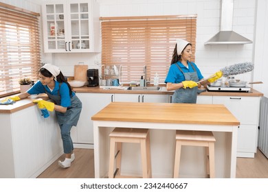 Two Asia woman in workwear maid cleaning home and holding dusting brush in her hand and wiping with microfiber cloth in kitchen room at home