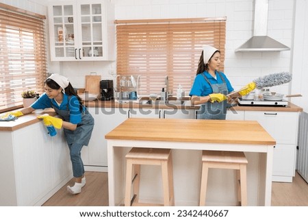 Two Asia woman in workwear maid cleaning home and holding dusting brush in her hand and wiping with microfiber cloth in kitchen room at home