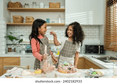 Two Asian adorable children sibling making a cake in kitchen at house. Happy Family, young little kid girls having fun spend leisure time together using ingredient bake bakery. Activity relationship.
