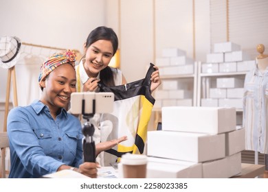 Two asian and african american woman business owner fashion designer cloth tailor creative working for new collection.Happy online store owner preparing an order for shipping . - Shutterstock ID 2258023385