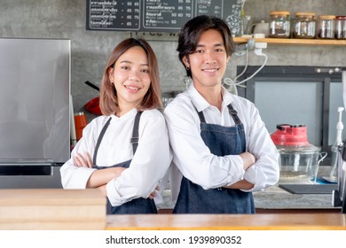 Two Asian Barista Or Coffee Maker Man And Woman Stand With Arm-crossed Or Confidence Action Also Look To Camera And Smile In Café Shop. Concept Of Happy Working With Small Business Together.  