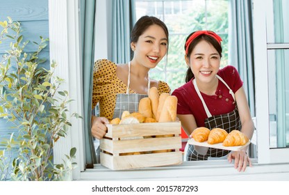 Two Asian beautiful female friends wearing aprons, standing and while opening window, welcome, happily smiling, serving breakfast baked bread, baguettes in the morning. Bakery Business, shop Concept - Powered by Shutterstock