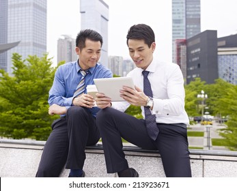 Two Asian Business Executives Using Ipad In City Park.