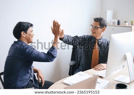 Two Asian business man smiling happy and giving high five at the office