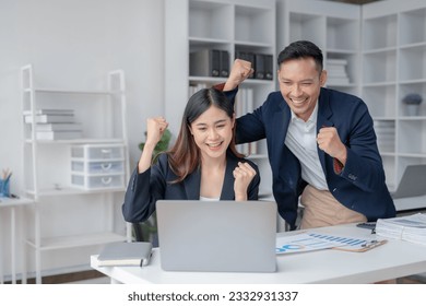Two Asian business people looking at laptop with arms raised showing happy expression at office. - Shutterstock ID 2332931337