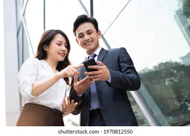 Two Asian business people using smartphone and talking together