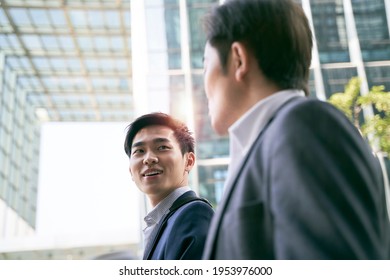 Two Asian Business People Walking Talking On Street In Modern City