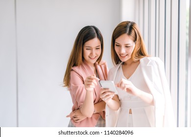 Two Asian Business Women Looking At The Smartphone Screen Using Smart Phone For Online Shopping, Internet.