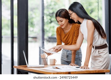 Two asian business women standing and talking about analyzing documents in workplace office - Powered by Shutterstock