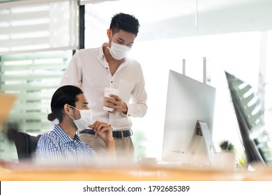 Two Asian Businessman Talk Discuss Their Work In Morning After Office Reopen Due To Coronavirus COVID-19 Pandemic. They Wear Protective Face Mask To Prevent Infection. New Normal Office Life Concept.