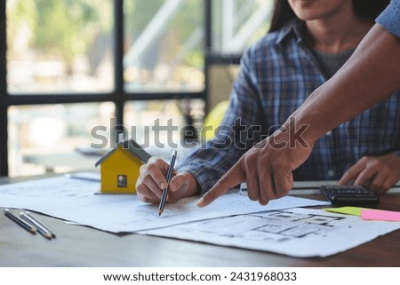 Two Asian businesspeople or architects are describing architectural house model in their office together for the construction of housing estate project in prime location the location is perfect.